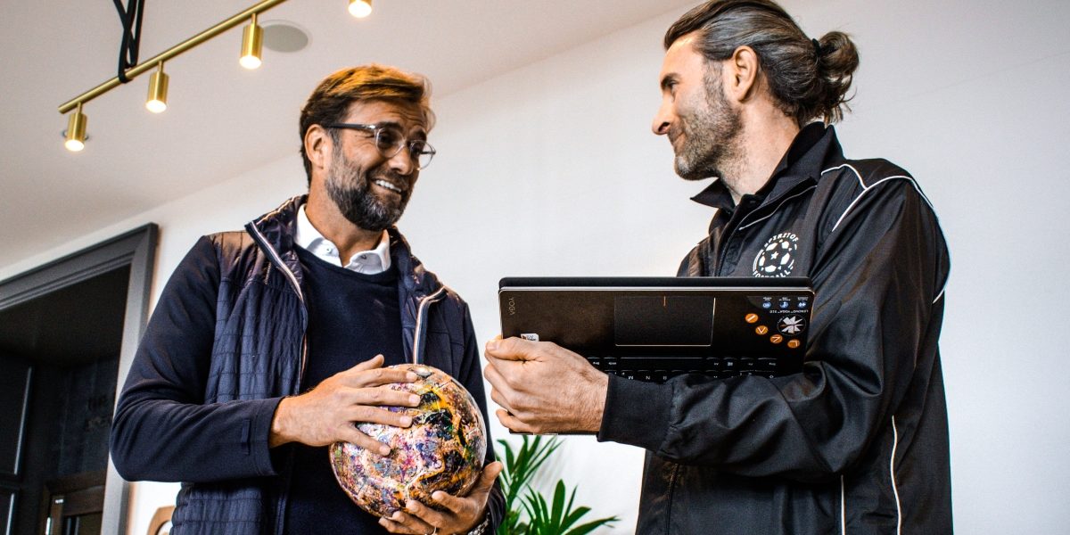 Spirit of Football's Präsident Andrew Aris (rechts) zeigt Jürgen Klopp auf einem Laptop Bilder der FairPlay-Projektreihe, die durch Klopp im Herbst 2015 und seiner ersten Unterschrift auf dem FairPlay-Ball ins Leben gerufen wurde. Foto: Phil Wake